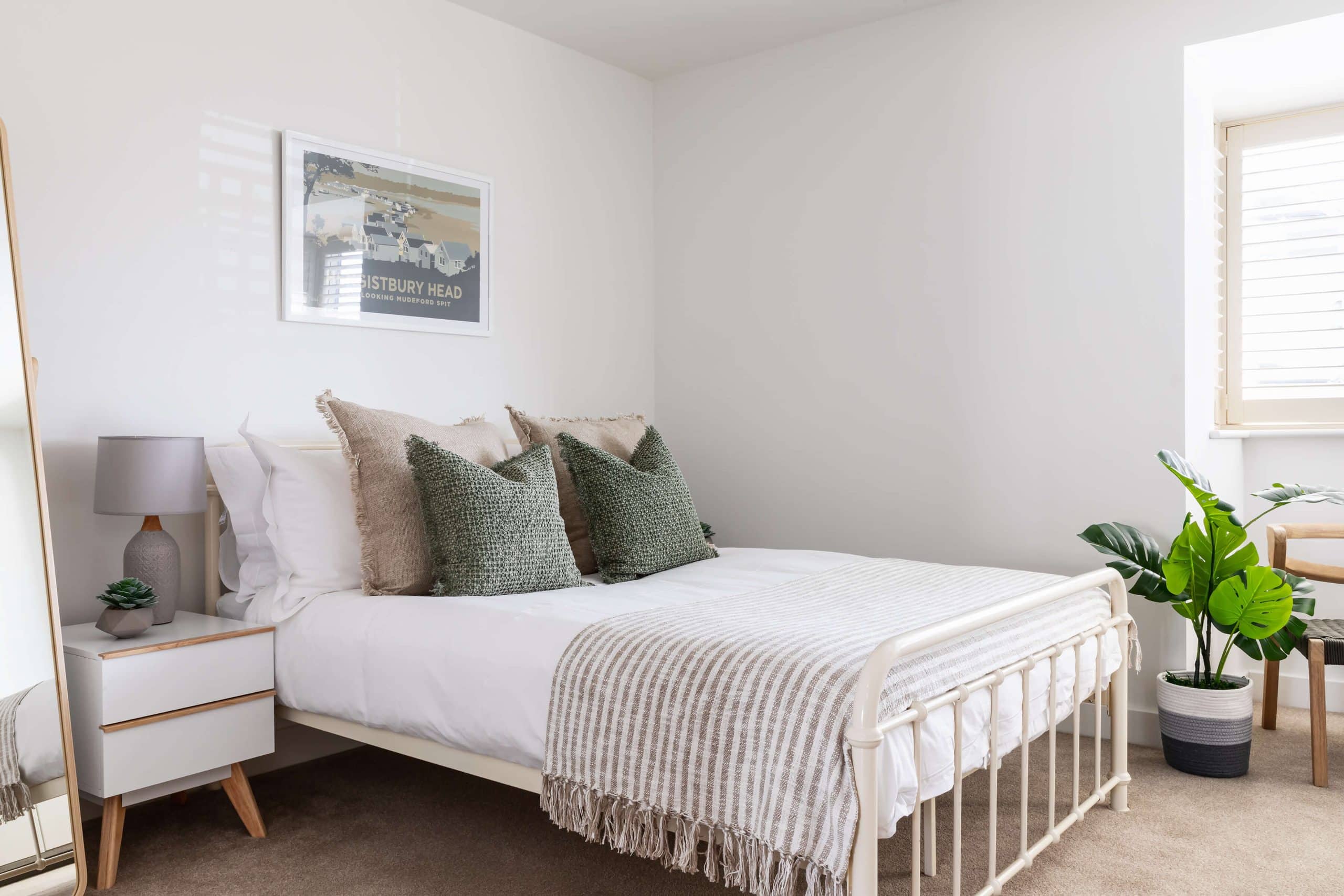 Neutral bedroom of white, grey, and muted greens with artwork of location surrounding Dorset Airbnb