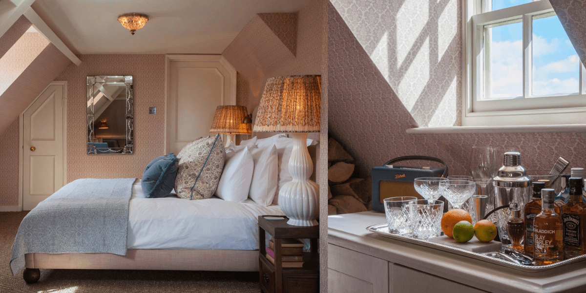 Attic double bedroom with muted pink walls and bed with bedding and muted blue accents, illuminated with large overhanging windows and warm bedside lighting
