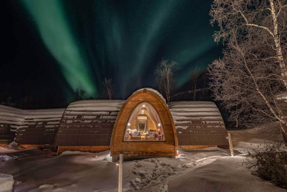 Kirkenes Snowhotel in Norway. Cabin in the snow amongst a forst with colour Northern lights in the nightsky