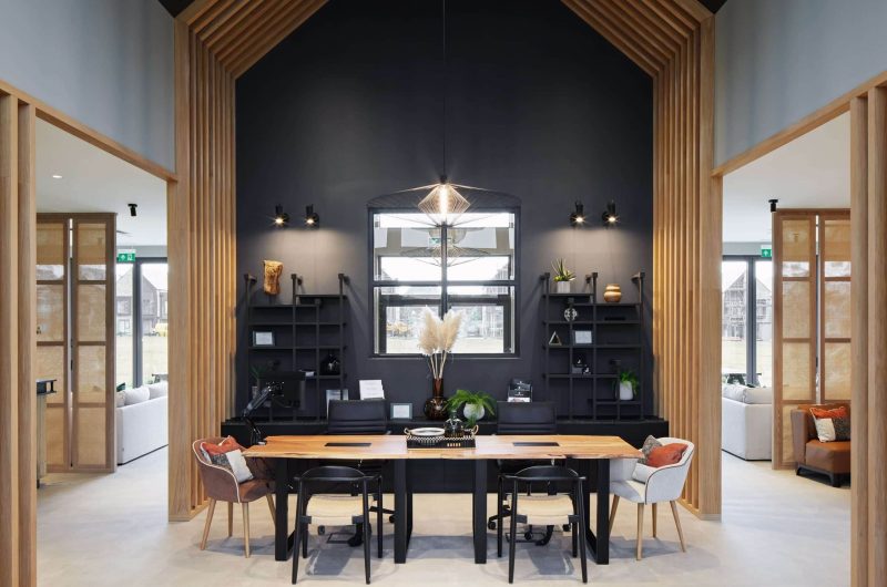Entrance of marketing space with 6 chairs around an oak table, with black shelving behind and a wooden paneled archway framing the space