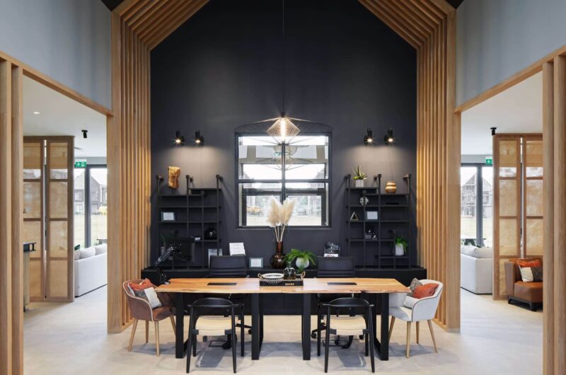 Entrance of marketing space with 6 chairs around an oak table, with black shelving behind and a wooden paneled archway framing the space