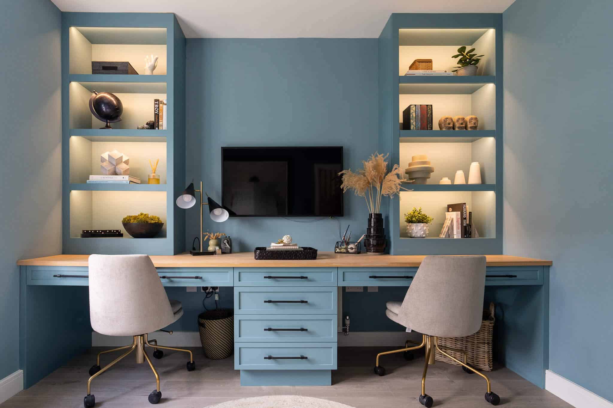 A picture of a blue bespoke desk in a study, with a car on the left and right and shelving enhanced with lighting