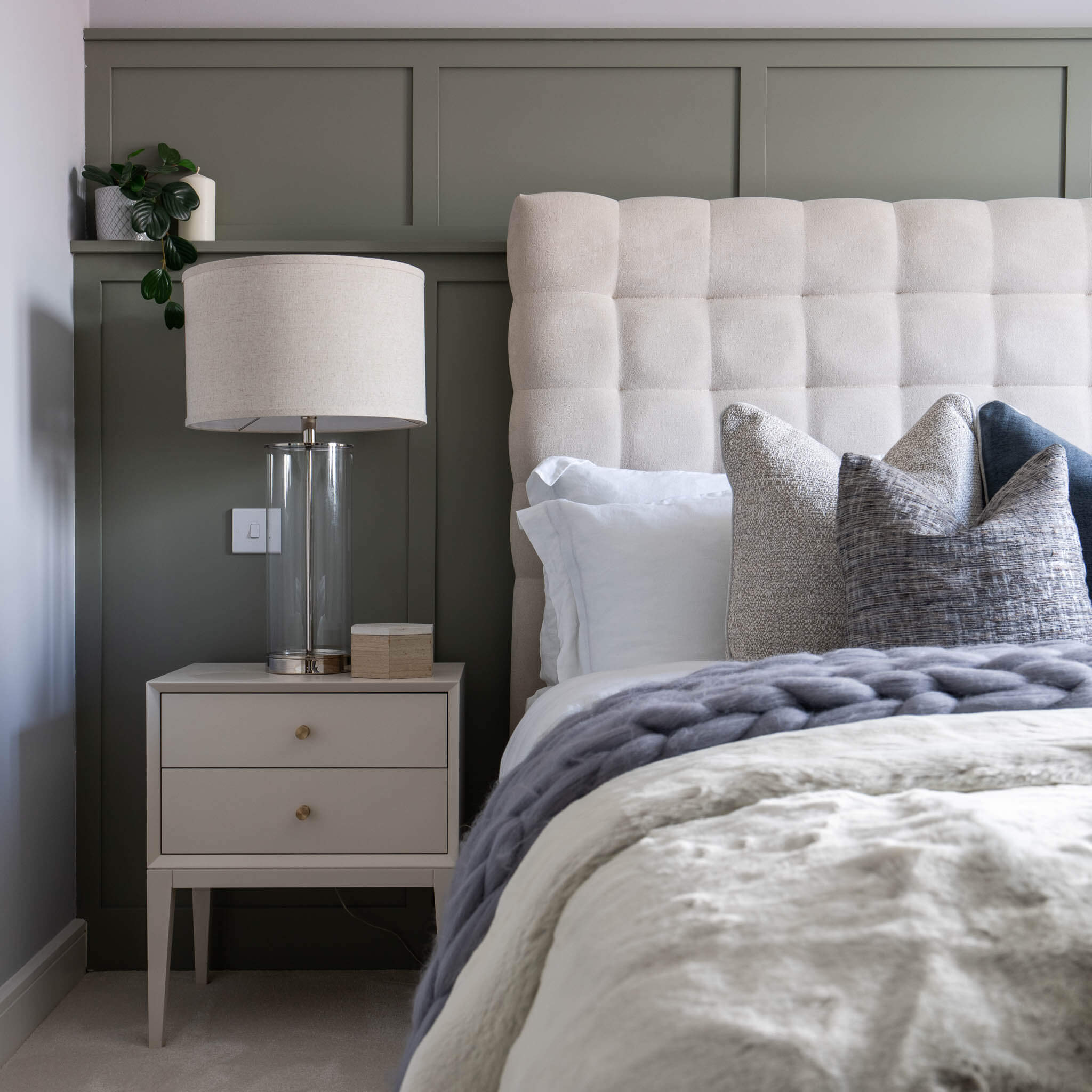 A picture of a bed with wall panelling behind, and a bedside table with a lamp switched off